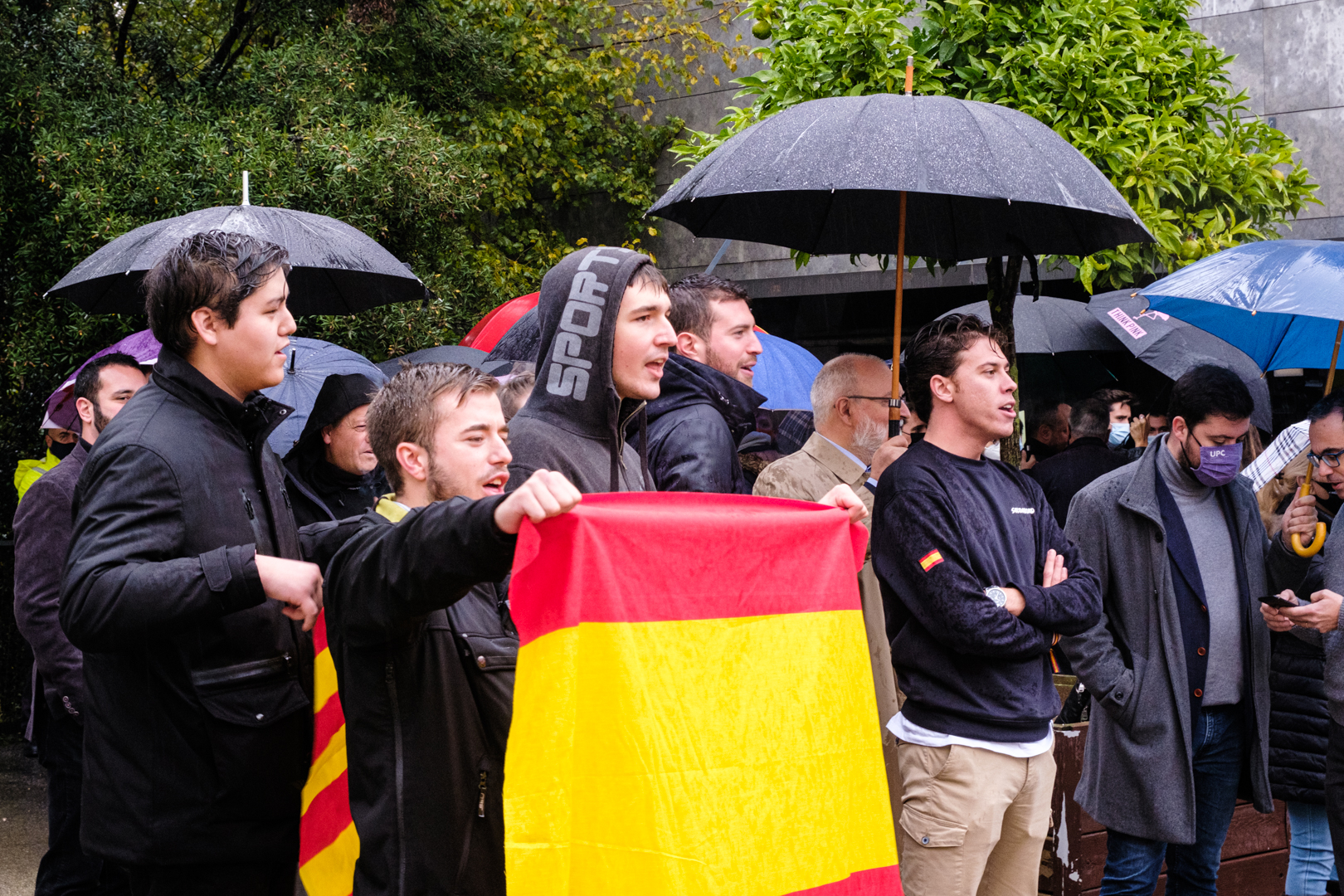 Alberto Tarradas (Vox), en primer pla i els braços creuats i quatre nois sostenen una bandera espanyola